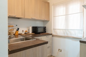 A kitchen with wooden cabinets, a stainless steel sink, a microwave, and a window with curtains. - Apartment 'La Dimora Di Pienza in Val D'Orcia' with Wi-Fi (Pienza)
