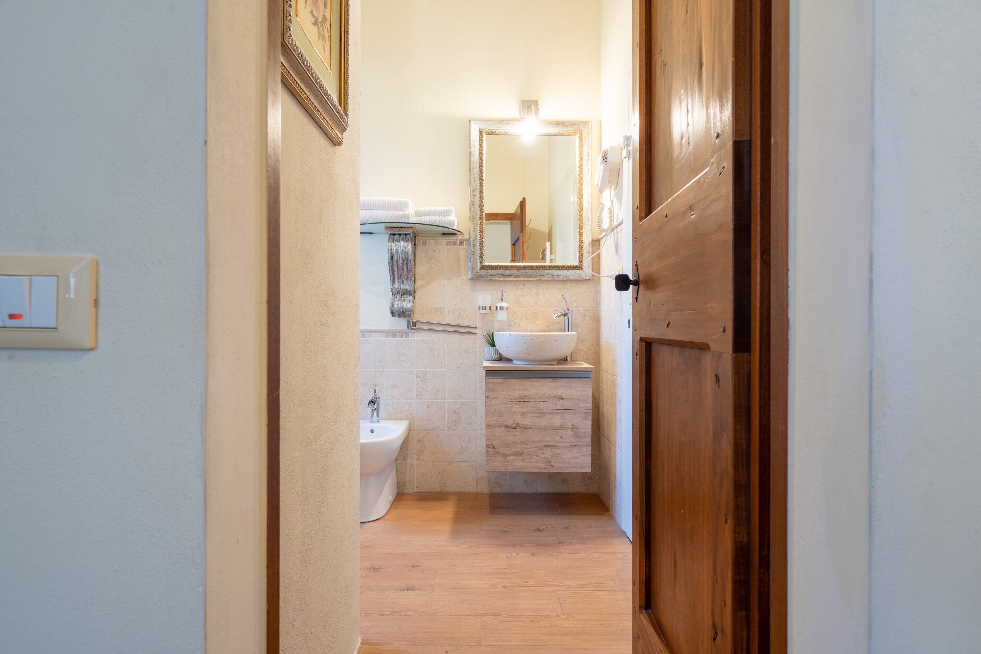 A narrow hallway leading to a bathroom with a sink, mirror, and towel rack.
