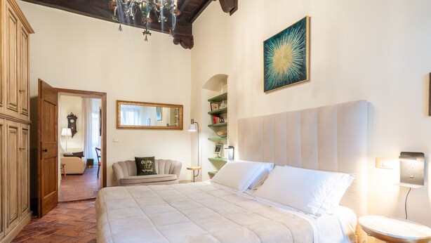 Un dormitorio con una cama grande, un armario de madera, un espejo, una araña y una lámpara de pared.