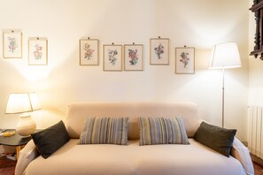 Een kamer met een bank, kussens, een lamp en bloemrijk kunstwerk in een lijst aan de muur.