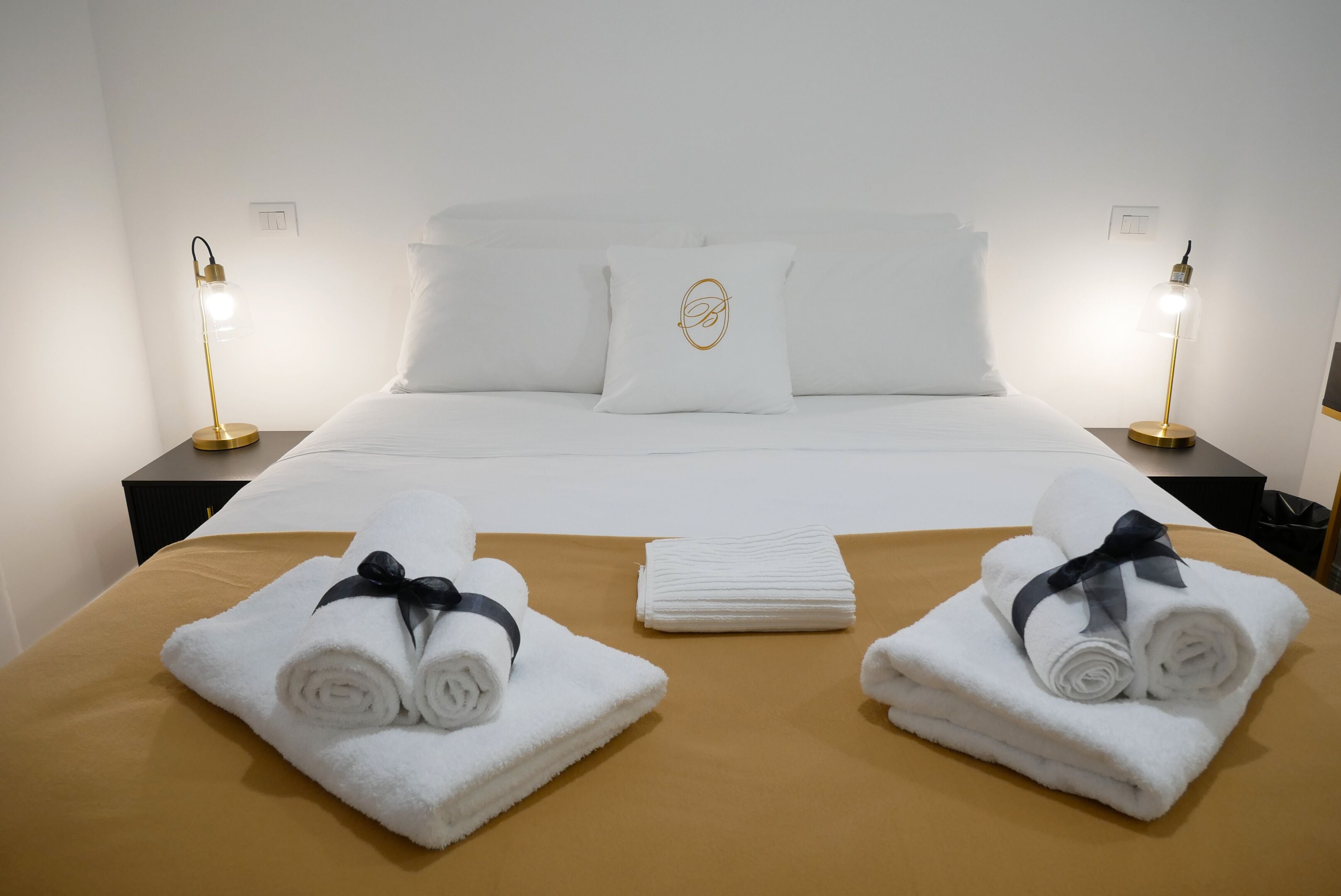 Una habitación de hotel con una cama bien hecha, dos lámparas de noche y toallas sobre la cama.
