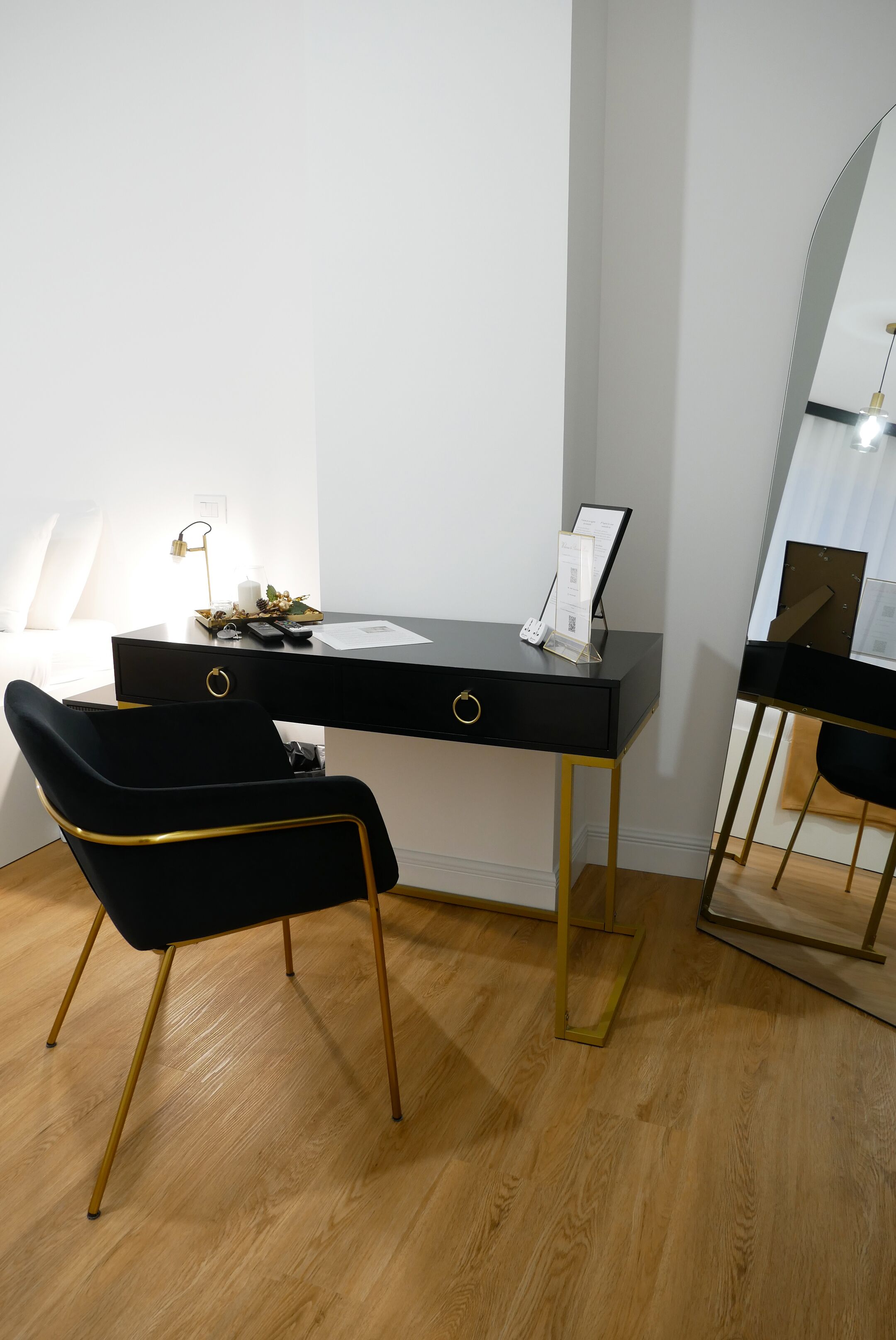 A modern room with a black desk, a black chair with gold accents, a mirror, and a small plant on the desk.
