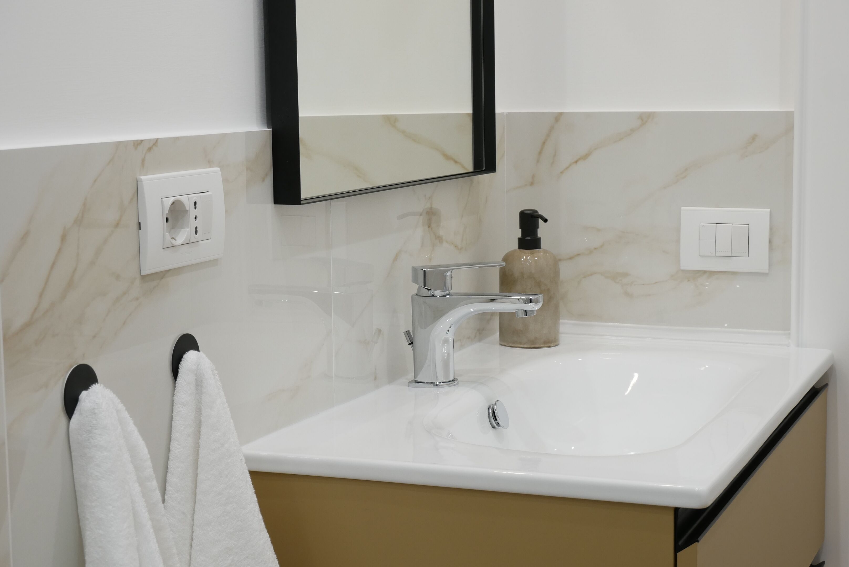 A bathroom with a white sink, a mirror, a black towel, and a soap dispenser.