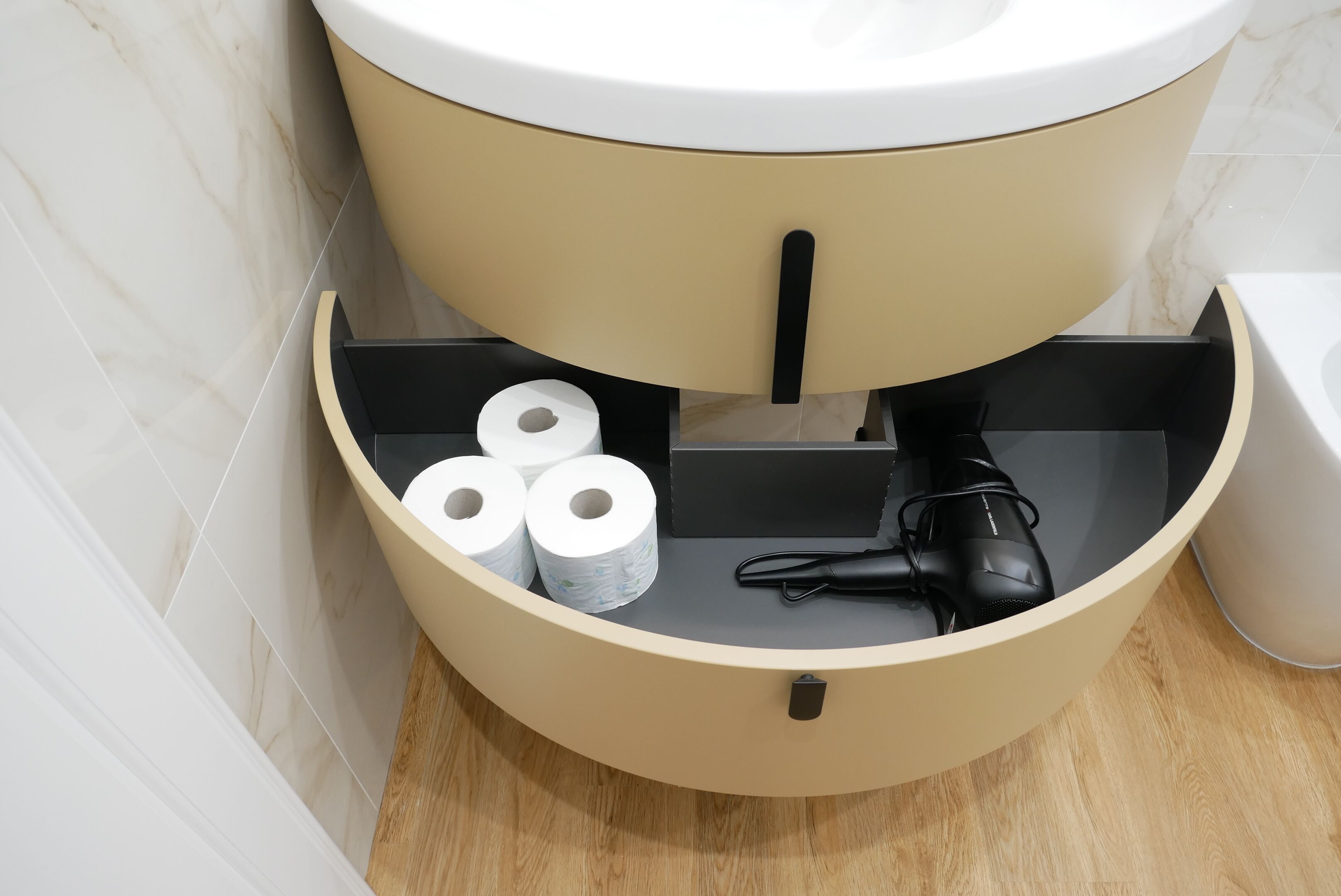 A toilet with a beige tank, a black toilet paper holder, and a black hairdryer.