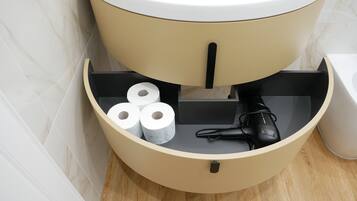 A toilet with a beige tank, a black toilet paper holder, and a black hairdryer.