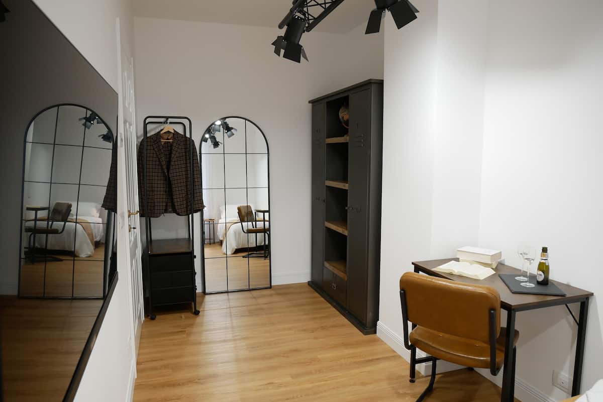 A room with a wooden floor, a brown leather chair, a desk with a bottle and glasses, and a wardrobe.
