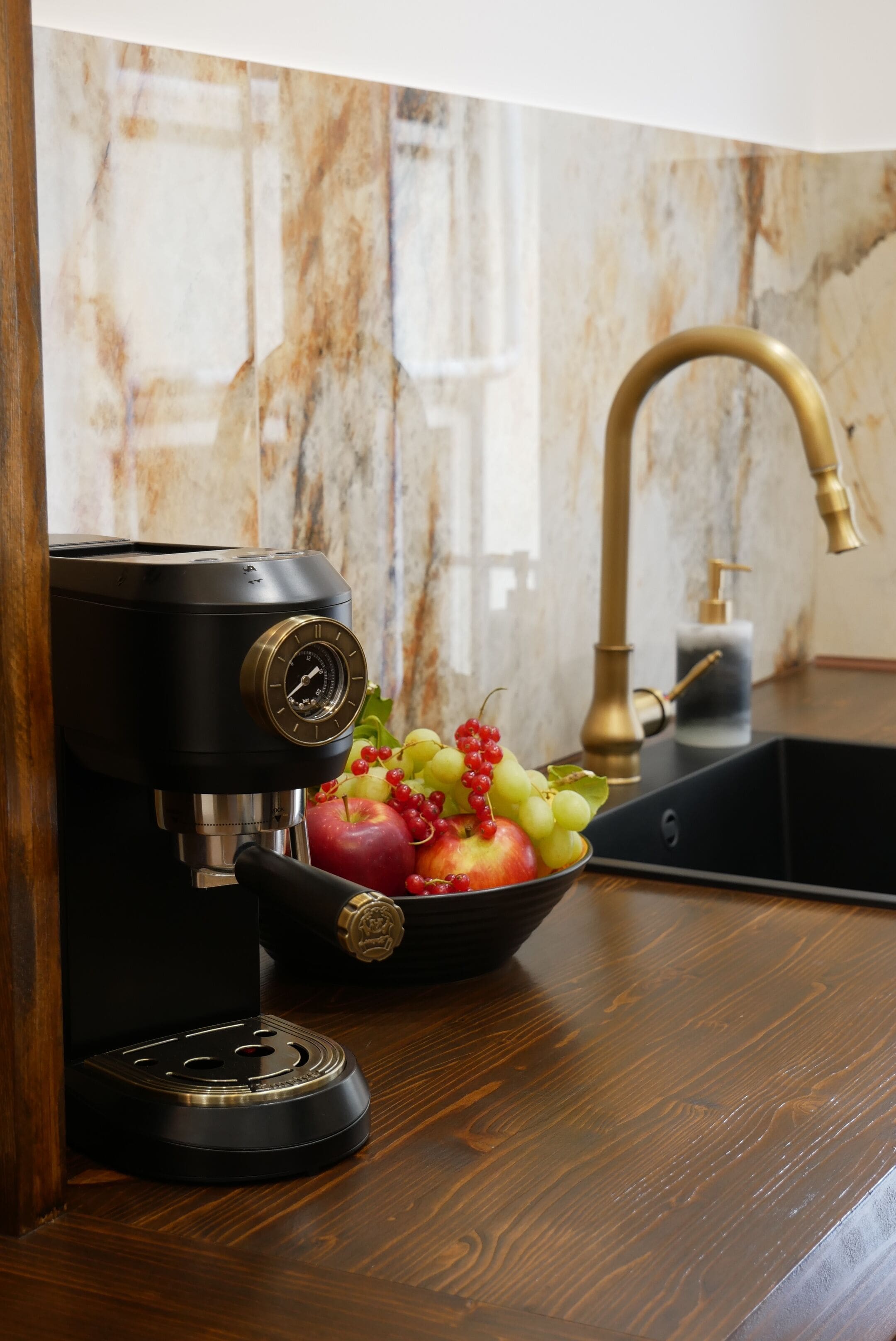 Una cocina con cafetera, un lavamanos y un cuenco de fruta.