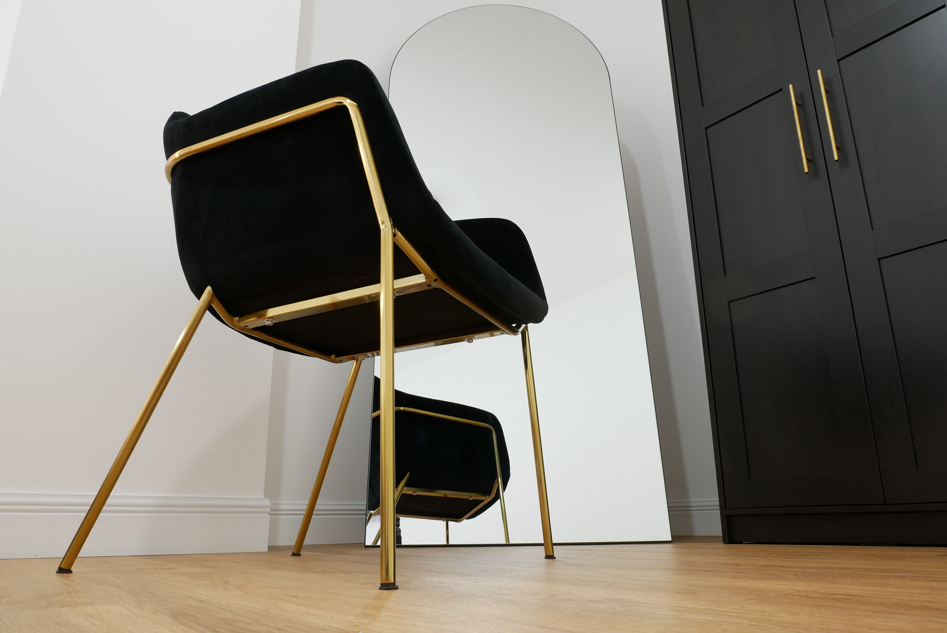 Una silla negra con patas doradas en una habitación con suelo de madera y un armario negro.
