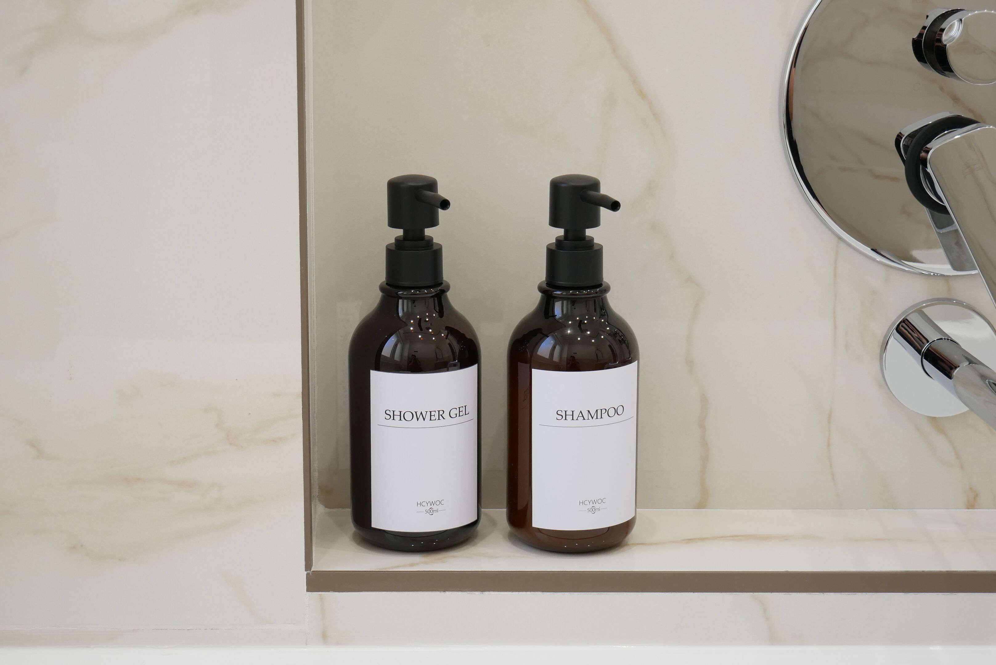 Two bottles of shower gel and shampoo on a marble countertop.