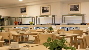 Een eetruimte met meerdere tafels en stoelen, een buffet met diverse gerechten en lijstjes aan de muur.