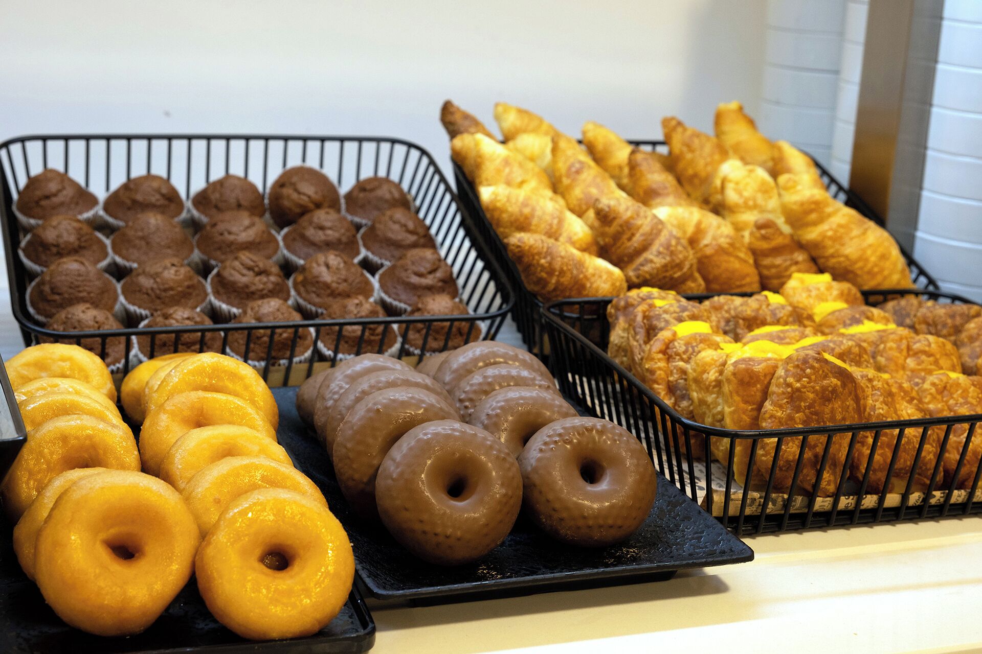 Tabletts mit Backwaren, darunter Muffins, Croissants und Donuts.