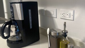 A black coffee maker on a white countertop, a salt and pepper shaker set, a bottle of oil, and a wall socket. - Charming Studio Apartment in Prado Santa Marta 3. (Santa Marta)