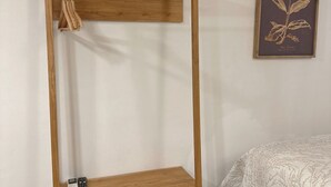 A wooden wardrobe with two shelves and a hanging rod, a small bedside table, and a framed botanical print on the wall. - Charming Studio Apartment in Prado Santa Marta 3. (Santa Marta)