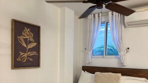 A bedroom with a bed, a ceiling fan, a window with curtains, and a framed botanical illustration on the wall. - Charming Studio Apartment in Prado Santa Marta 3. (Santa Marta)