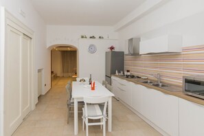 Eine moderne Küche mit weißen Schränken, einer gestreiften Spritzschutzwand und einem Essbereich mit einem weißen Tisch und Stühlen.