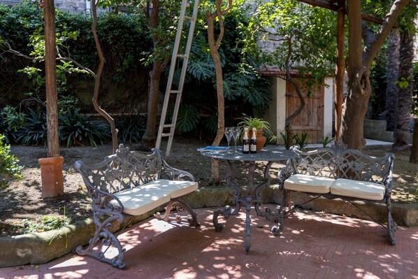 Eine Terrasse mit schmiedeeisernen Möbeln, einer Leiter und Kübelpflanzen.
