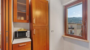 Una cocina con armarios de madera, microondas y ventana con vista a una colina.
