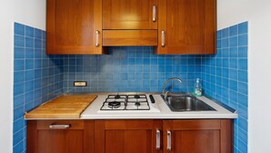 Una cocina con armarios de madera, estufa a gas, un lavamanos y salpicadero de azulejos azules.