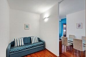 Ein Zimmer mit einer Couch, einem Esstisch mit Stühlen und einem Flur, der in ein weiteres Zimmer führt.