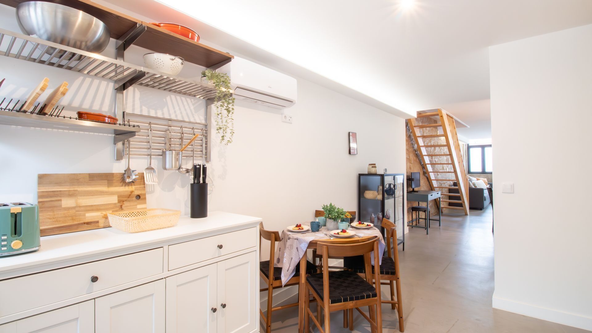 A modern kitchen with white cabinets, a wooden countertop, and a dining area with a table set for two.