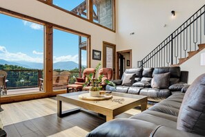 A spacious living room with a large window, a wooden coffee table, leather sofas, and a staircase. - Exceptional Mountain View*Indoor Pool*Game Room *Sleeps 12 (GATLINBURG)