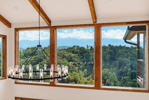 A room with large windows, a chandelier, and a view of a forested landscape. - Exceptional Mountain View*Indoor Pool*Game Room *Sleeps 12 (GATLINBURG)