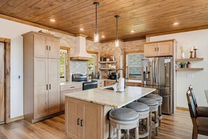 A modern kitchen with wooden cabinets, a central island with bar stools, stainless steel appliances, and pendant lighting. - Exceptional Mountain View*Indoor Pool*Game Room *Sleeps 12 (GATLINBURG)