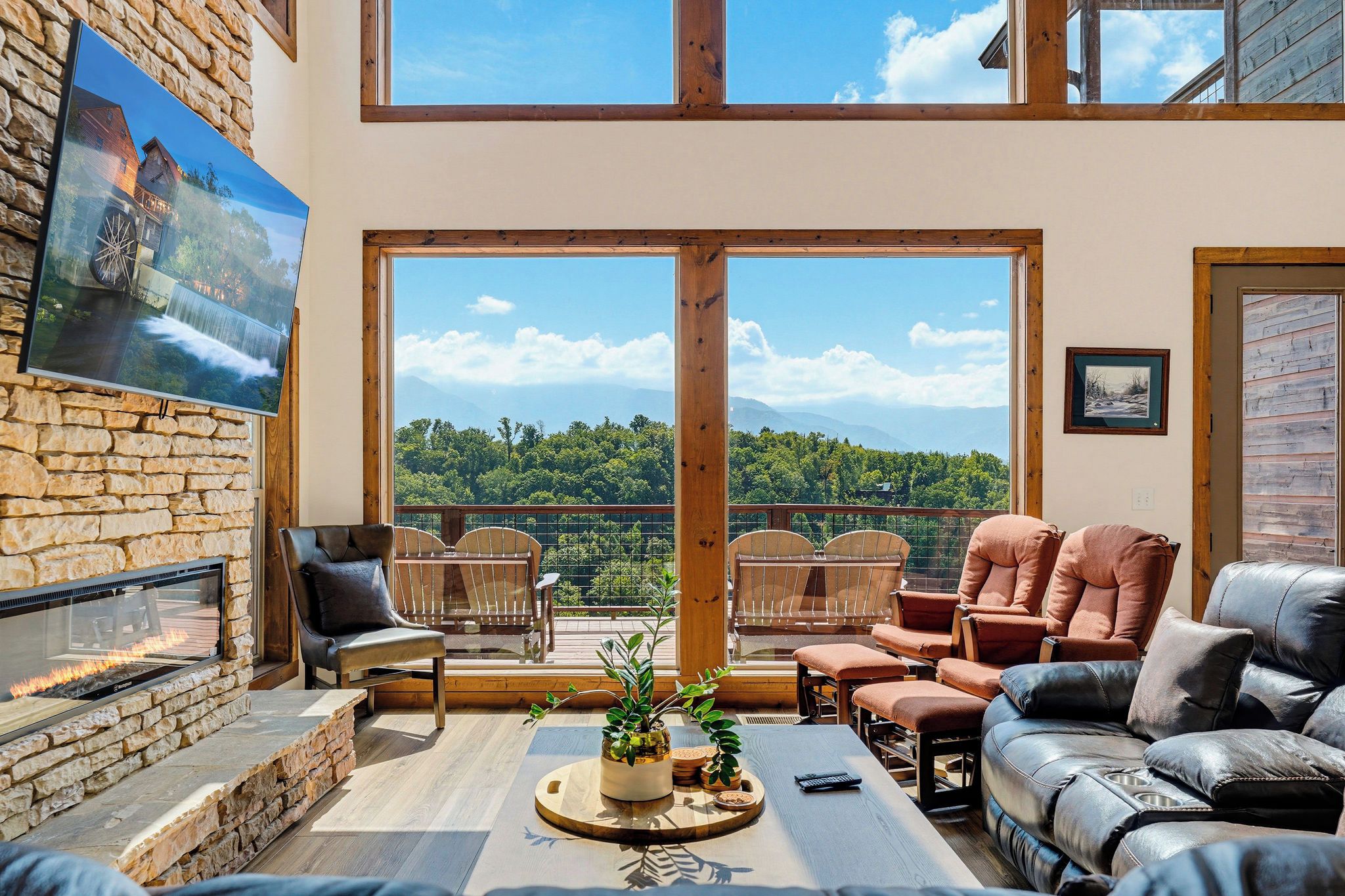 A spacious living room with a stone fireplace, leather sofas, and a large window offering a scenic view.