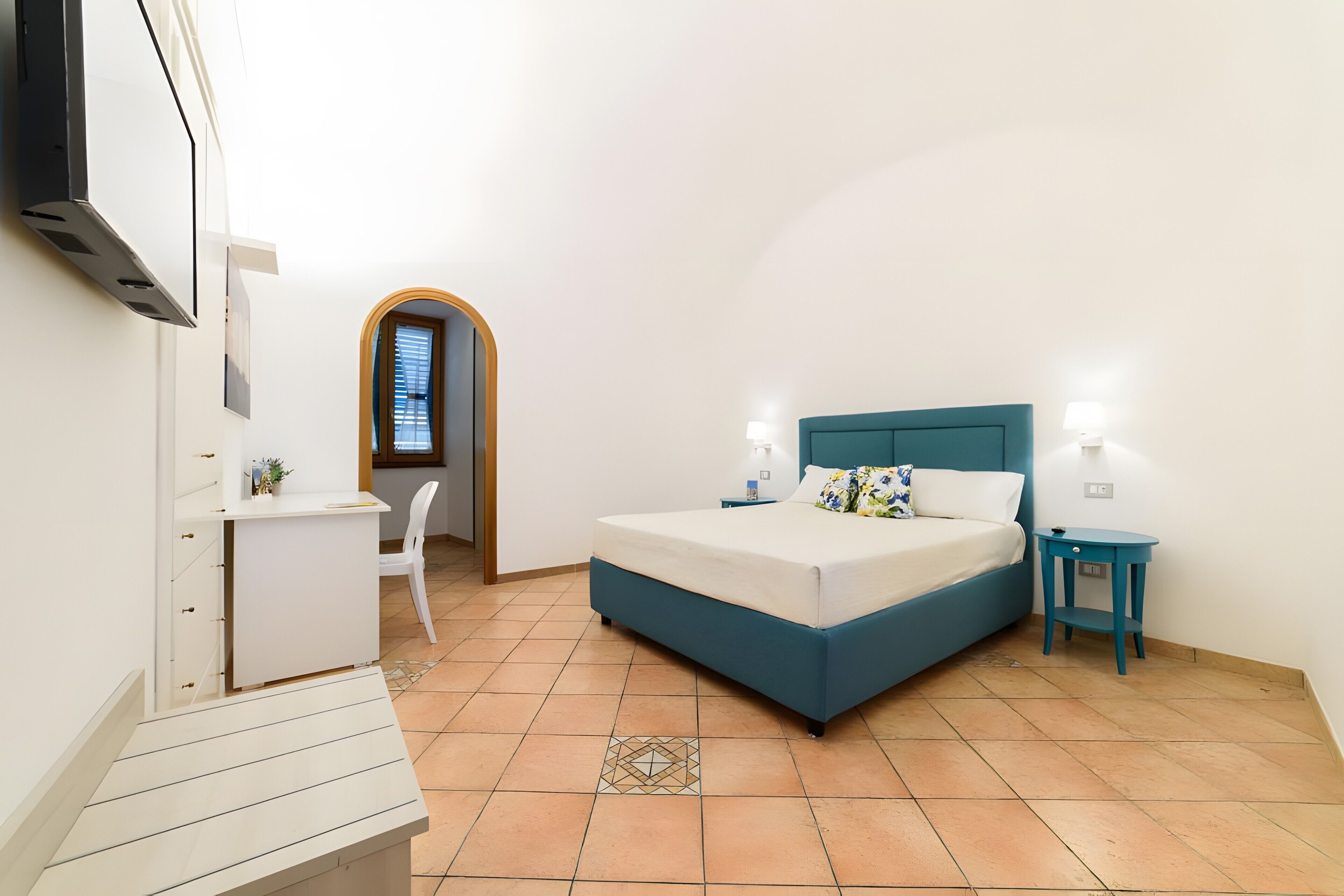 Un dormitorio con cama, mesitas de noche, escritorio, silla y ventana.
