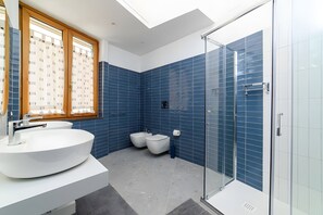Ein modernes Badezimmer mit Dachfenster, einem großen weißen Waschbecken, zwei Bidets und einer Duschkabine.