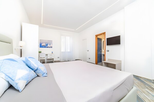 Ein modernes Hotelzimmer mit einem großen Bett, einem Schreibtisch, einem Sessel, einem Fernseher und einem Badezimmer.