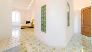 A hallway with patterned flooring, a bed, a green-framed window, and a wooden door. - 'Positano Luxury' Room with Balcony, Wi-Fi and Air Conditioning (Meta)
