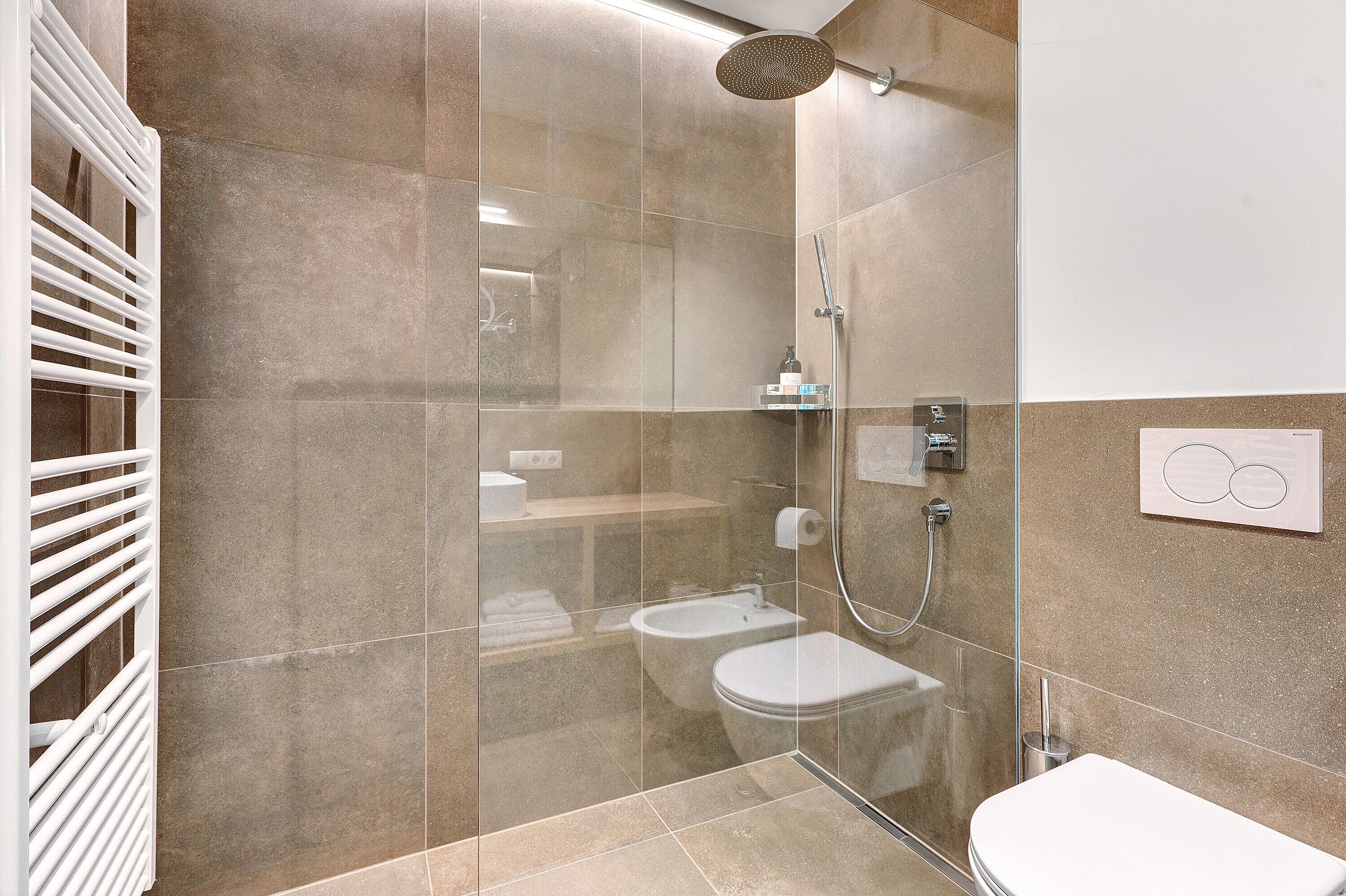A modern bathroom with a glass-enclosed shower, a toilet, and a bidet.