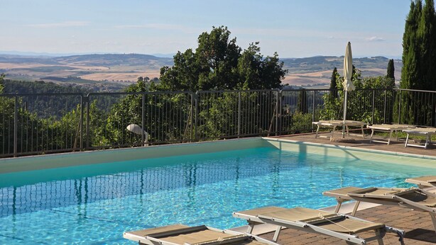 Una piscina con sillones de descanso, un área cercada y vistas a colinas distantes.