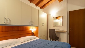 Un dormitorio con cama, cabecera de madera, armarios, una silla, un espejo y una puerta.