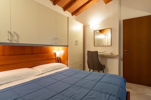 Ein Schlafzimmer mit einem Bett, einem Holzkopfende, Schränken, einem Sessel, einem Spiegel und einer Tür.