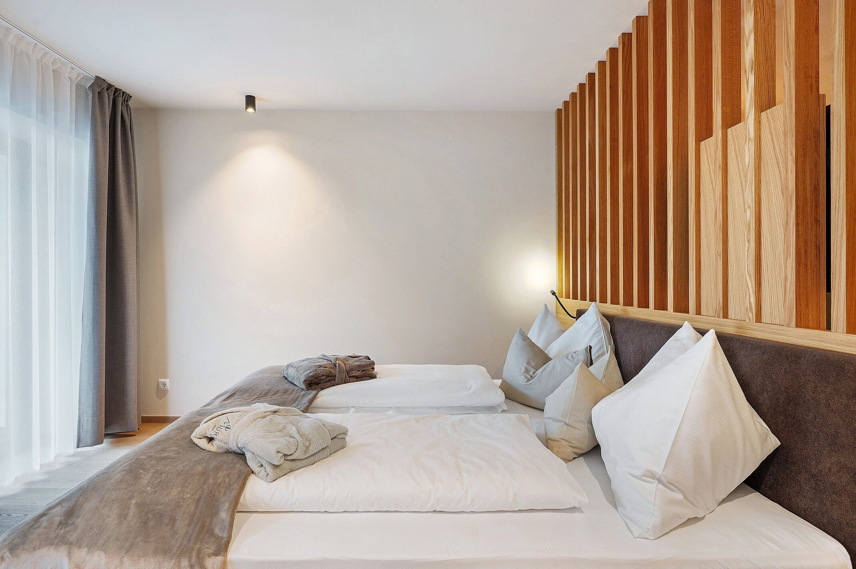 Une chambre d’hôtel avec un lit, des oreillers, une tête de lit en bois et une fenêtre avec des rideaux.