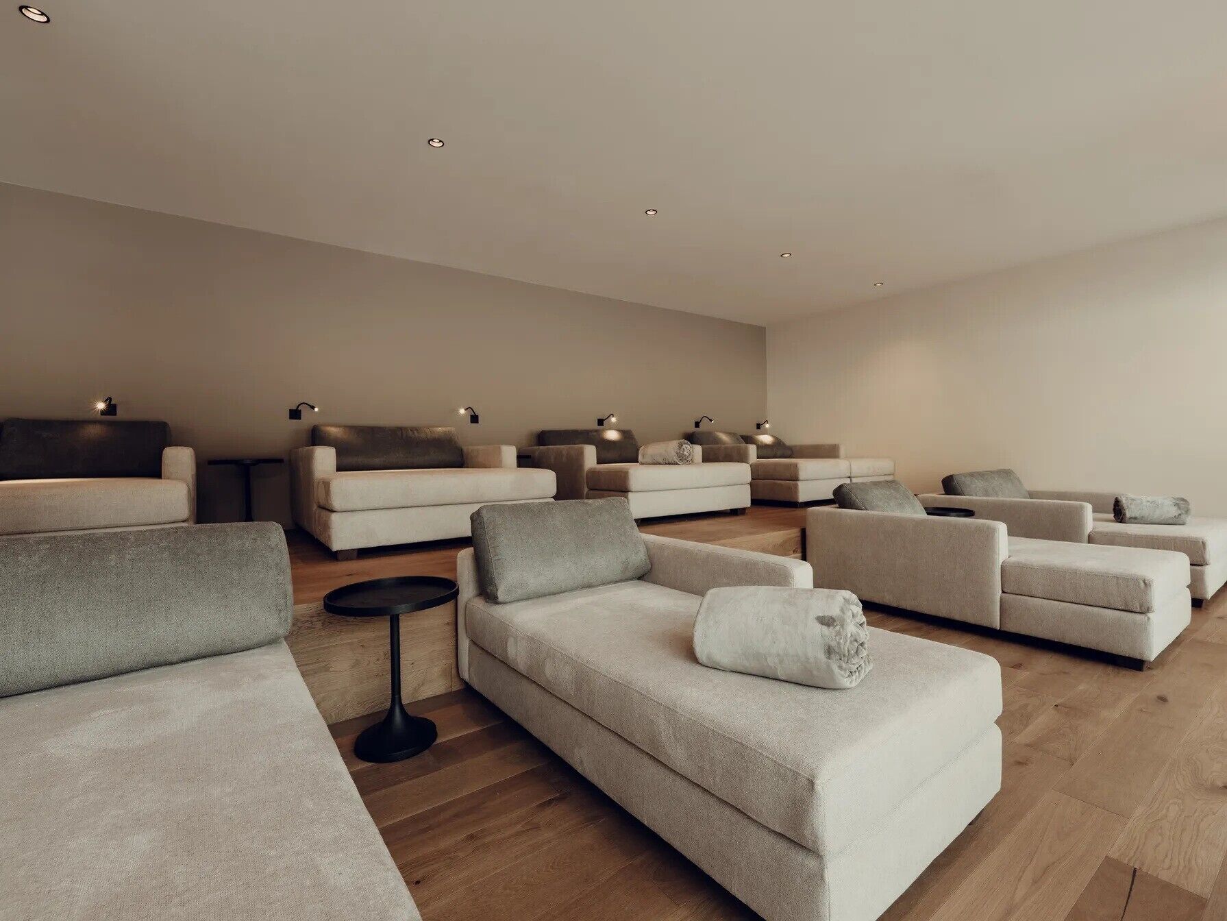 Un salon moderne avec plusieurs canapés disposés en forme de U, une petite table d’appoint ronde de couleur noire et un éclairage encastré au plafond.