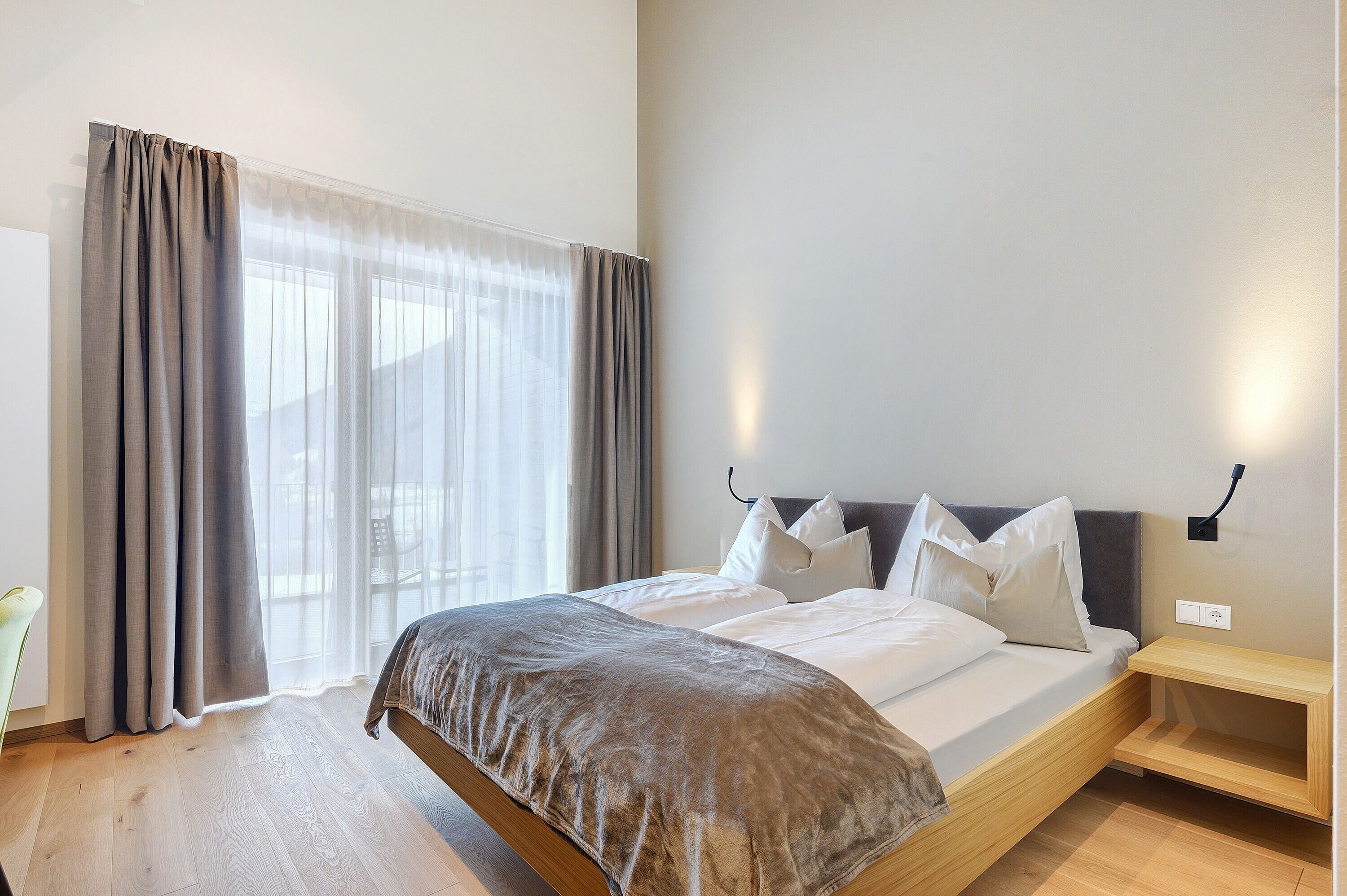 A bedroom with a bed, curtains, a bedside table, and a wall-mounted light.