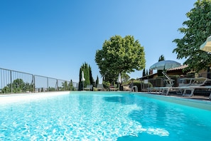 Una piscina con lettini, un grande albero e un edificio con tetto a cupola.