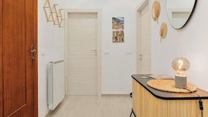 Ein Flur mit Holztür, Heizkörper, Wandspiegel und Tisch mit Lampe.