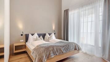 Un dormitorio moderno con una cama de madera, mesitas de noche y cortinas translúcidas.