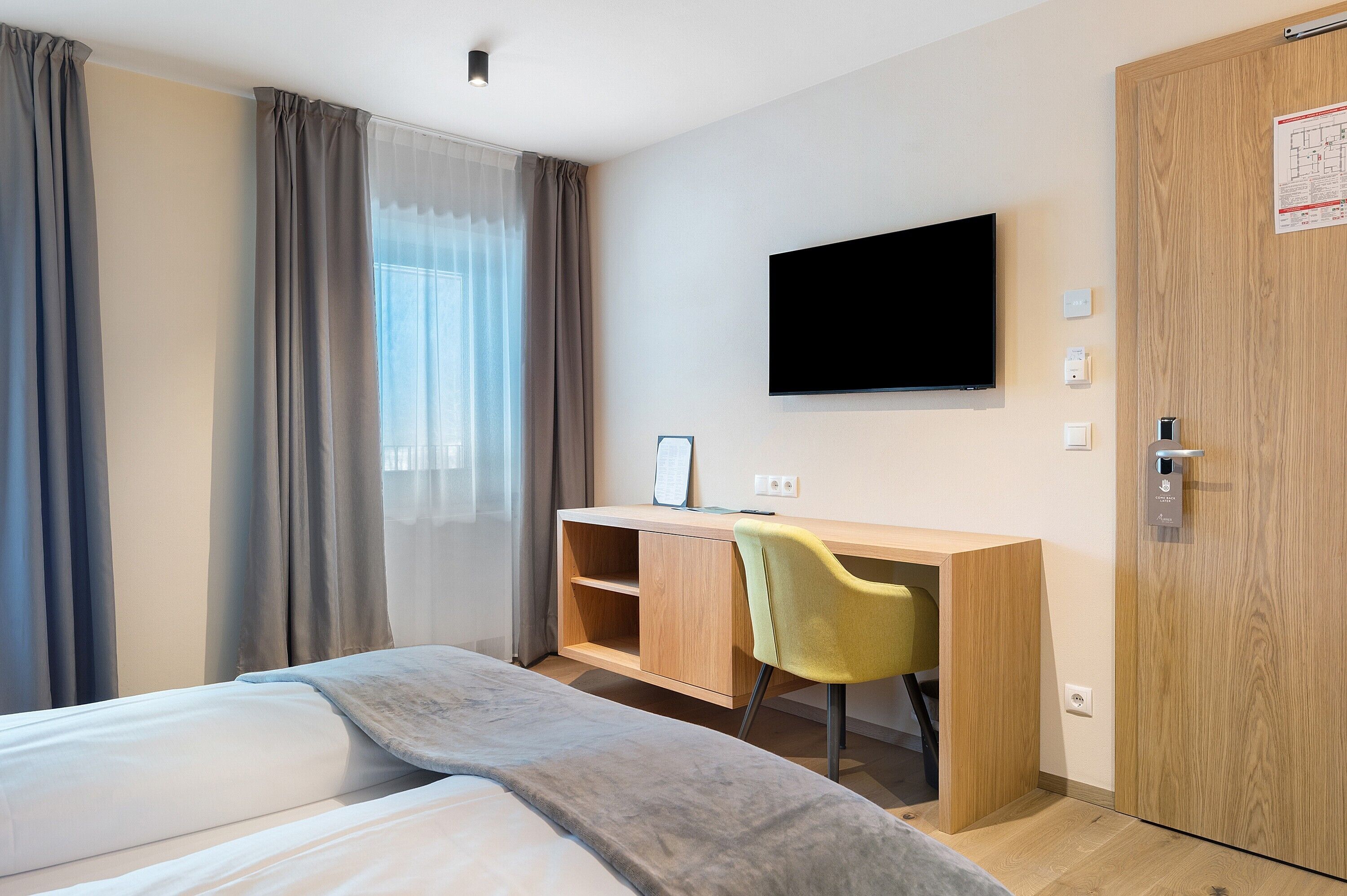 Ein Hotelzimmer mit einem Bett, einem Schreibtisch mit Stuhl, einem Fernseher und einem Kleiderschrank.