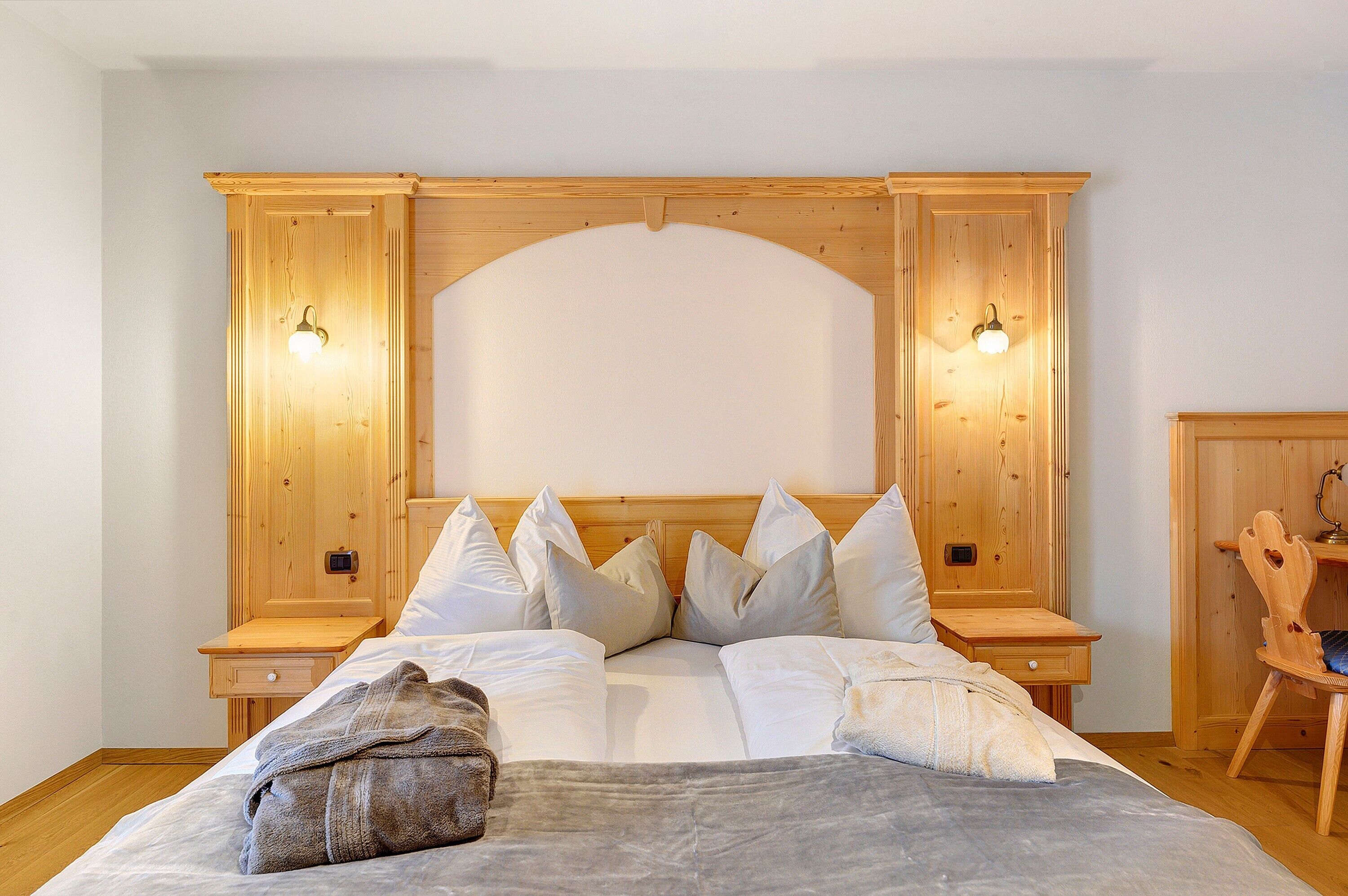 Une chambre à coucher avec une tête de lit en bois, un lit avec une literie blanche, deux tables de chevet et deux lampes fixées au mur.
