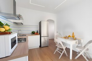 A modern kitchen with a gas stove, a refrigerator, and a dining area with a white table and chairs. - ‘Sorrento Luxury 1’ Apartment with Balcony, Wi-Fi, and Air Conditioning (Sorrento)