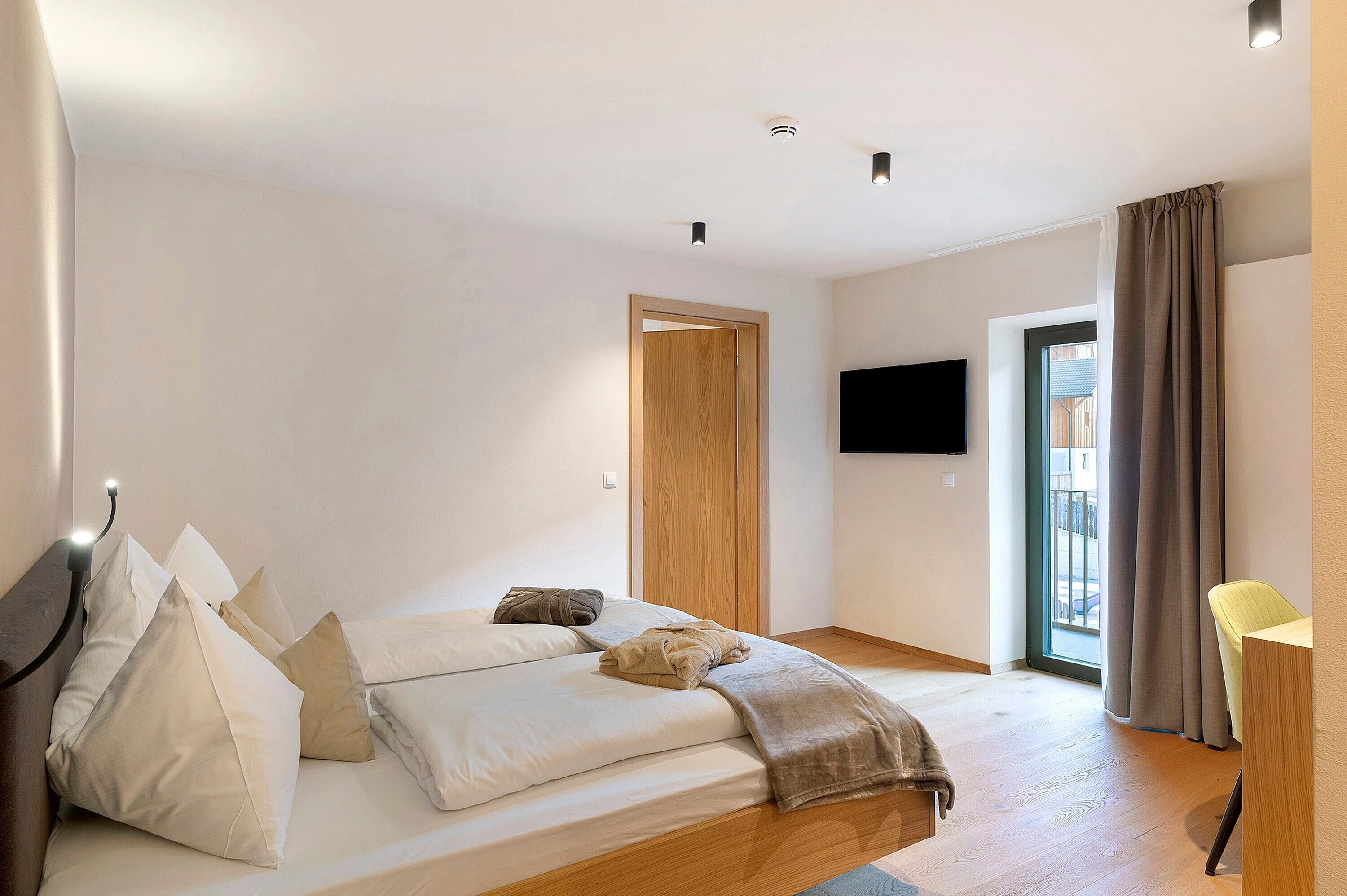 A modern bedroom with a bed, a TV, a wooden door, and a window with curtains.