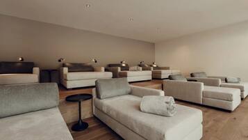 Ein modernes Wohnzimmer mit mehreren Sofas, die in U-Form angeordnet sind, einem runden schwarzen Beistelltisch und Einbau-Deckenleuchten.