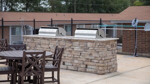 Une terrasse extérieure avec un barbecue en pierre, une table et des chaises.