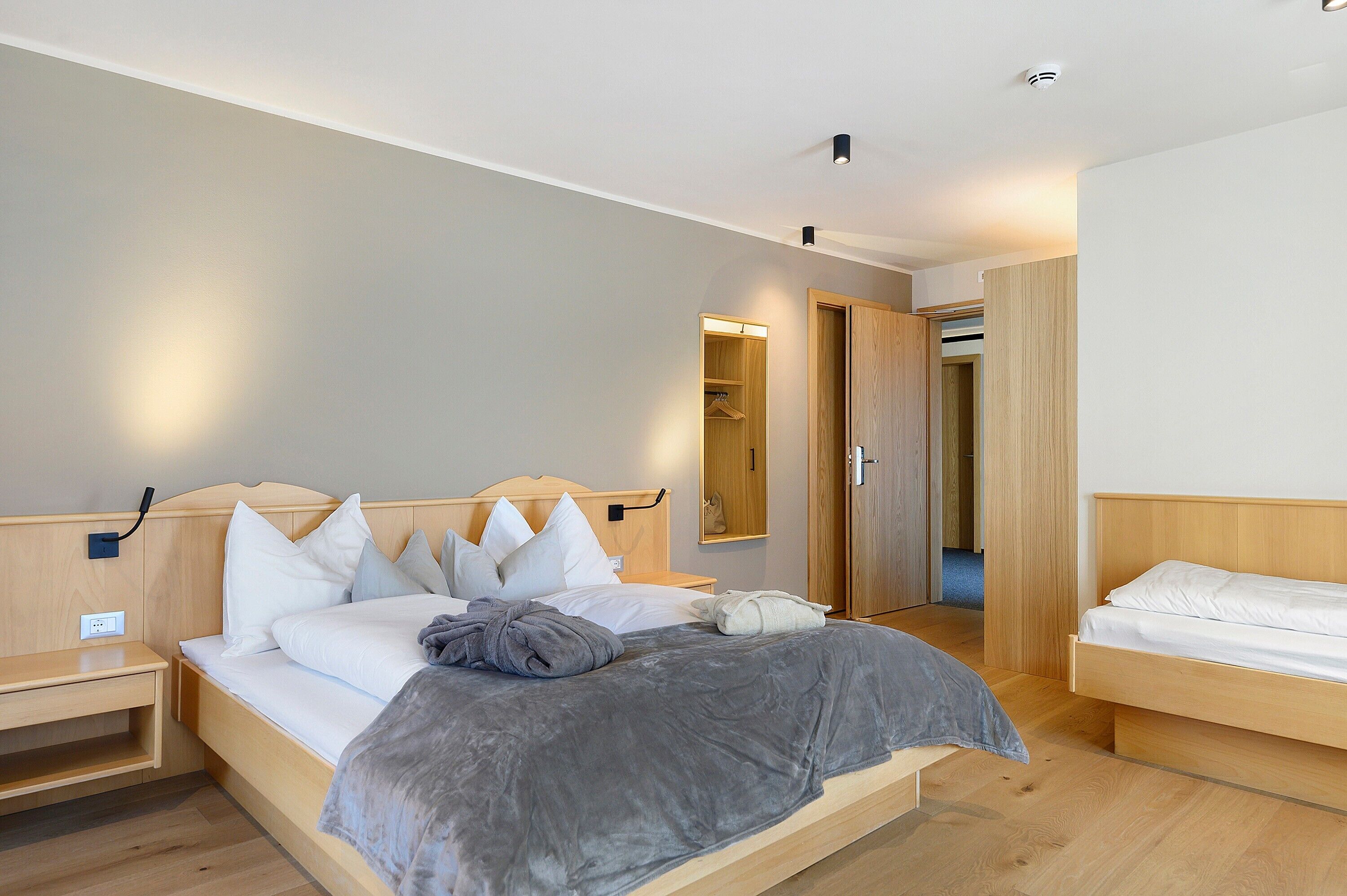 Une chambre d’hôtel moderne avec un lit en bois, une table de chevet, une armoire et un miroir.
