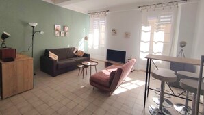 A living room with a sofa, a TV, a coffee table, a pink chair, a wooden cabinet, and a floor lamp.